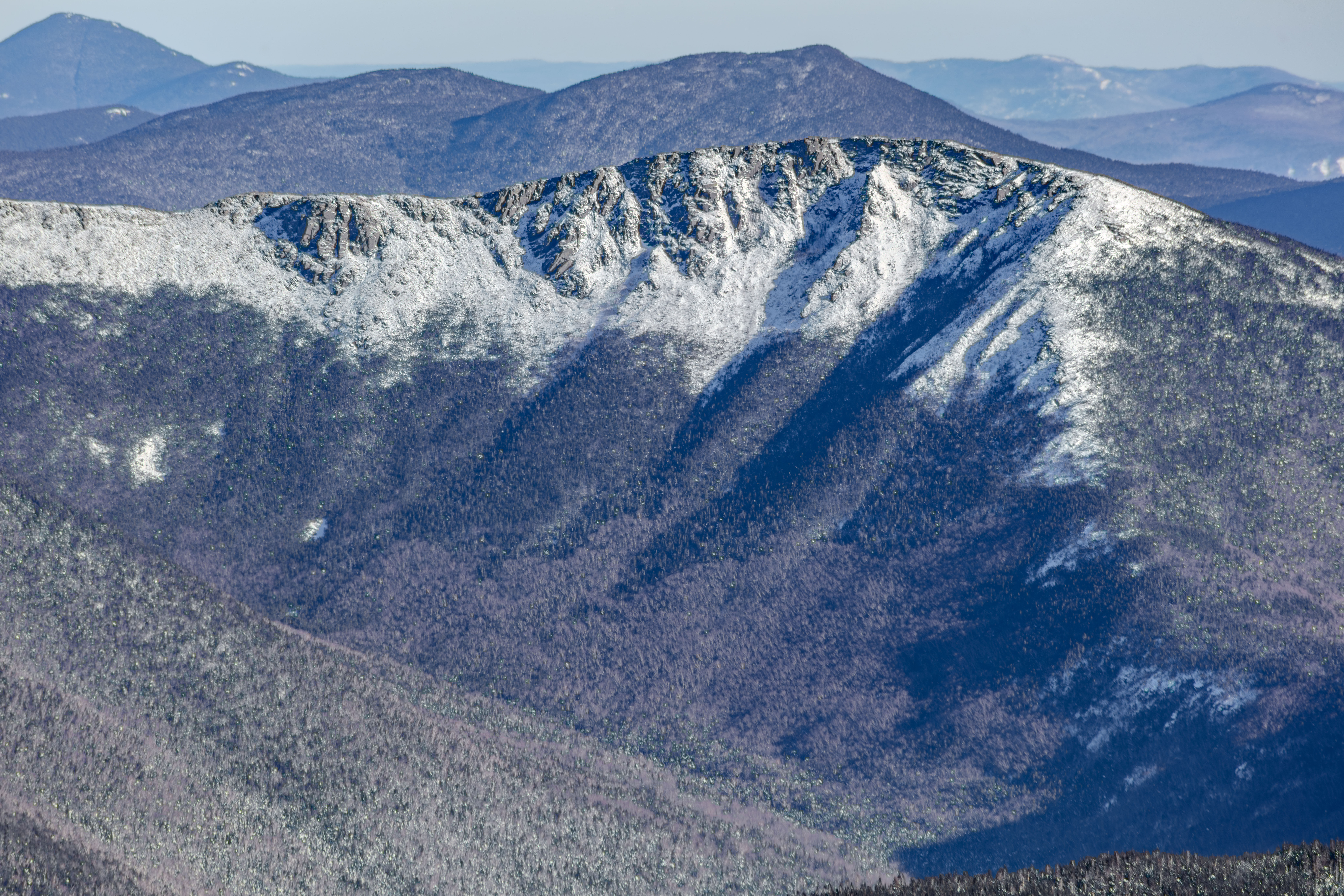 Snow-covered Bondcliff ridge with granite ledges and forest shadows in winter afternoon light