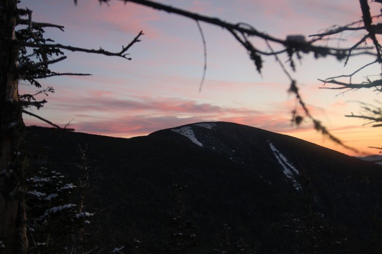 Carter Dome peak at sunset with snowy patches and silhouetted trees in winter