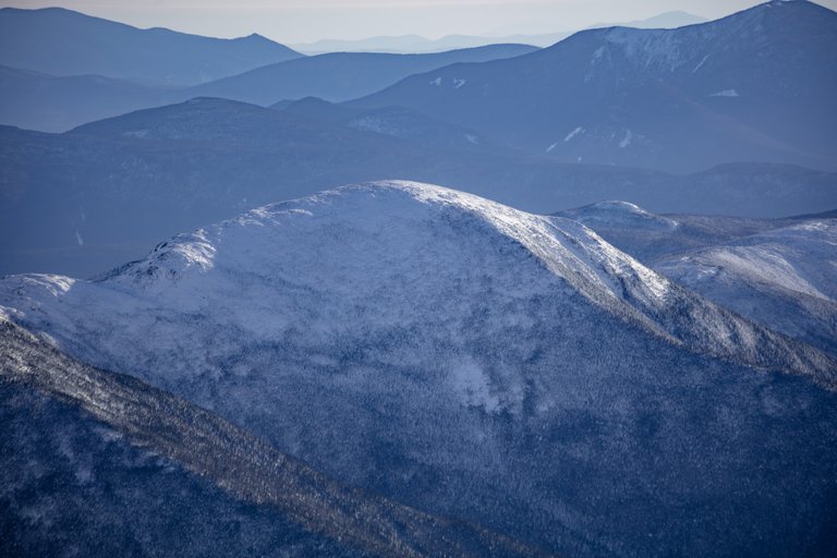 Snow-covered Mount Eisenhower summit in winter afternoon light with layered mountain ridges