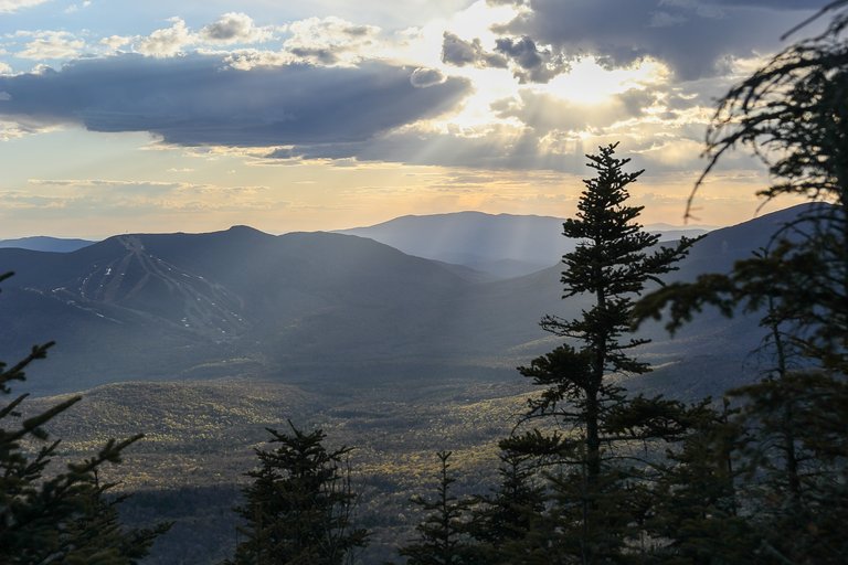 Mount Tecumseh at sunset with sun rays piercing clouds and forested valley below