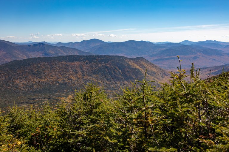 Fall landscape of Owls Head summit with colorful trees and distant mountain ridges under clear blue sky