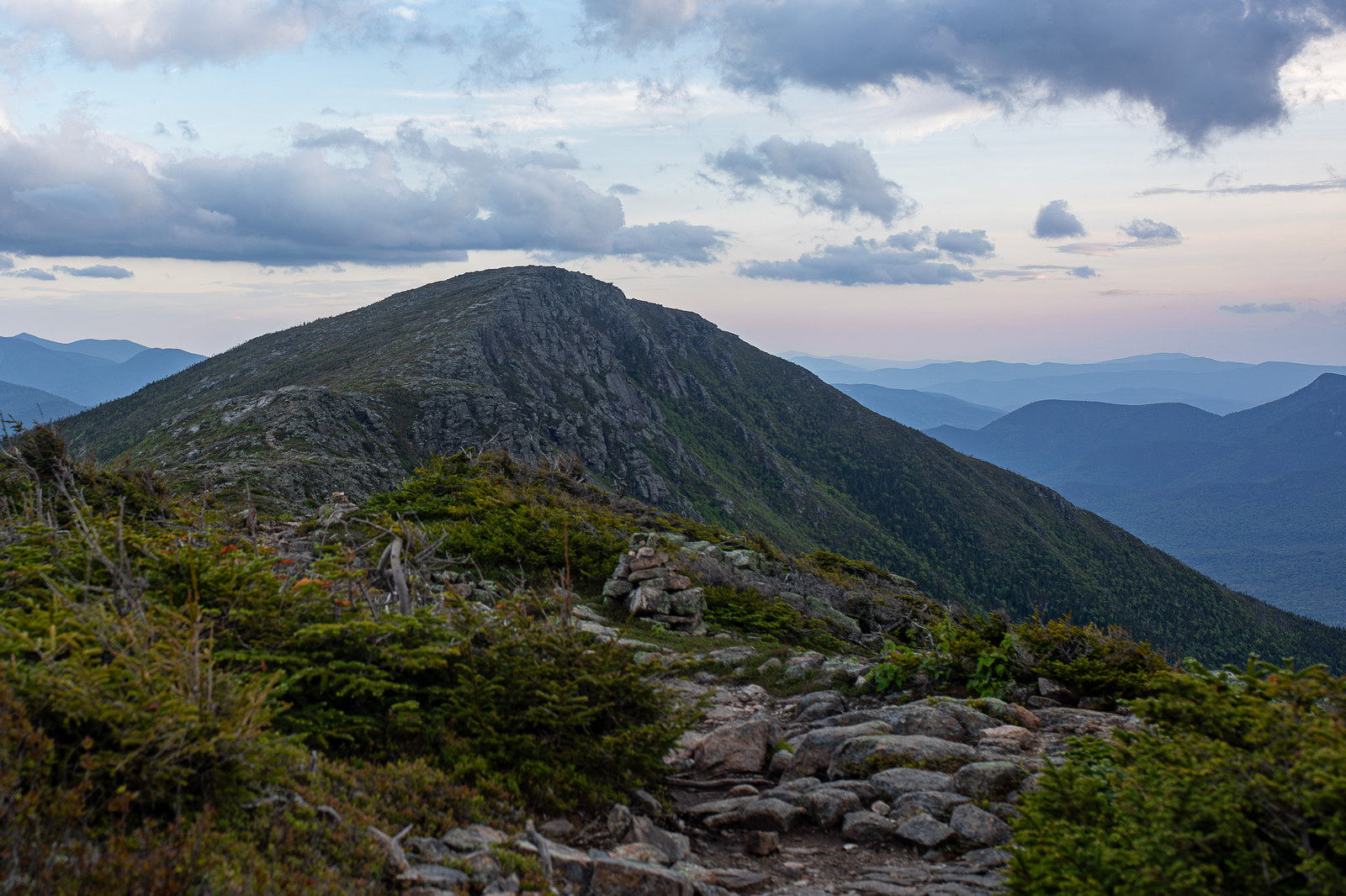 Bondcliff summit at dusk with rocky trail and distant mountain ridges in White Mountain National Forest