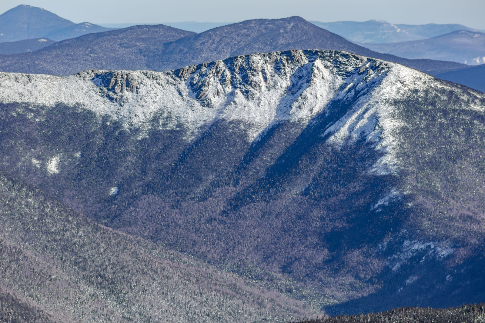 Snow-covered Bondcliff ridge with granite ledges and forest shadows in winter afternoon light