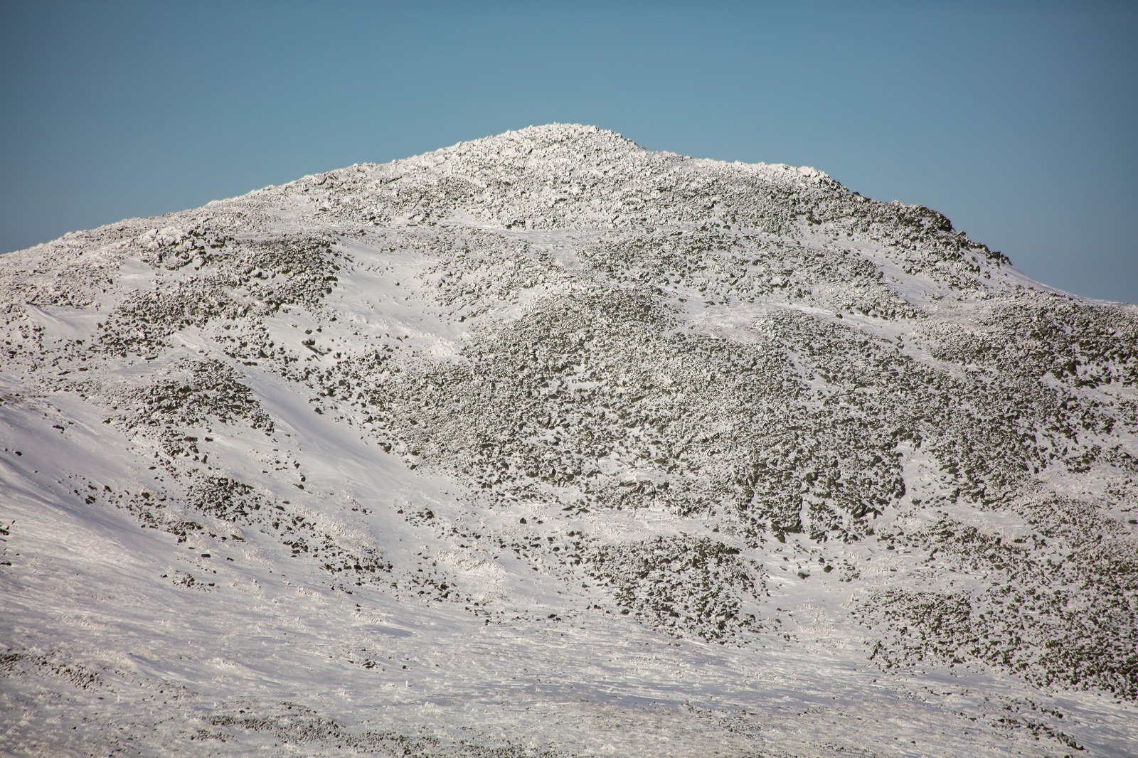 Snow-covered granite ledges on Mount Adams summit ridge under clear blue sky