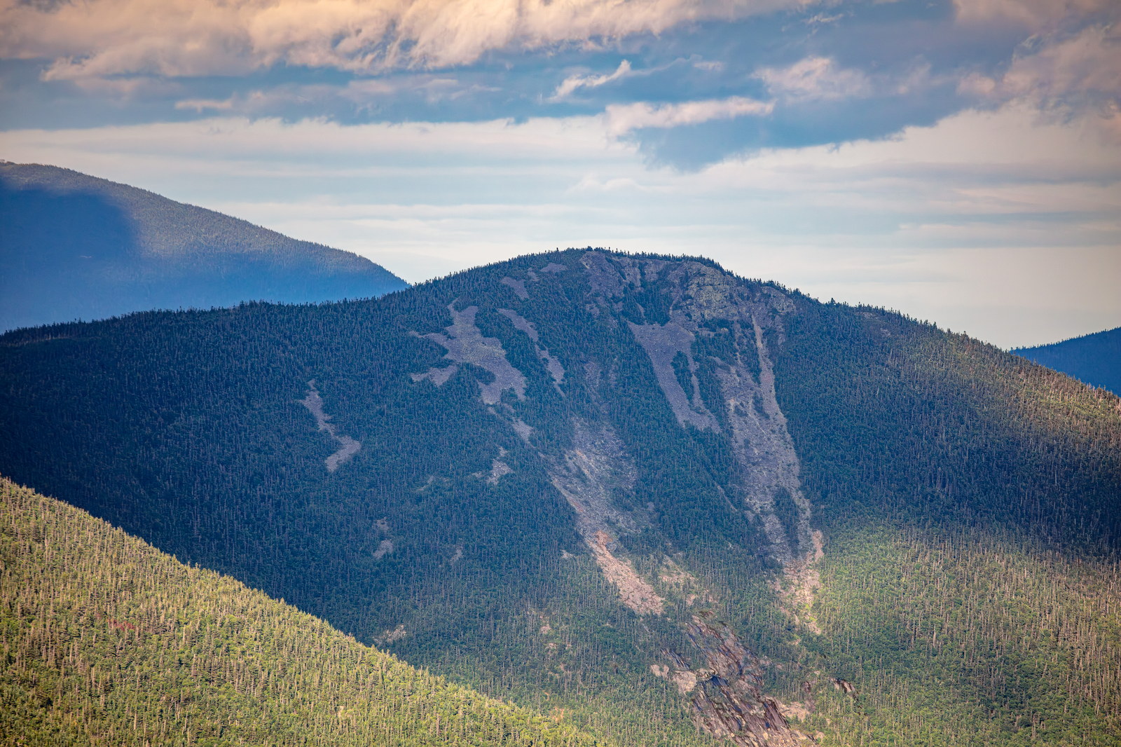 Mount Flume summit and alpine slopes under summer sunset with scattered clouds