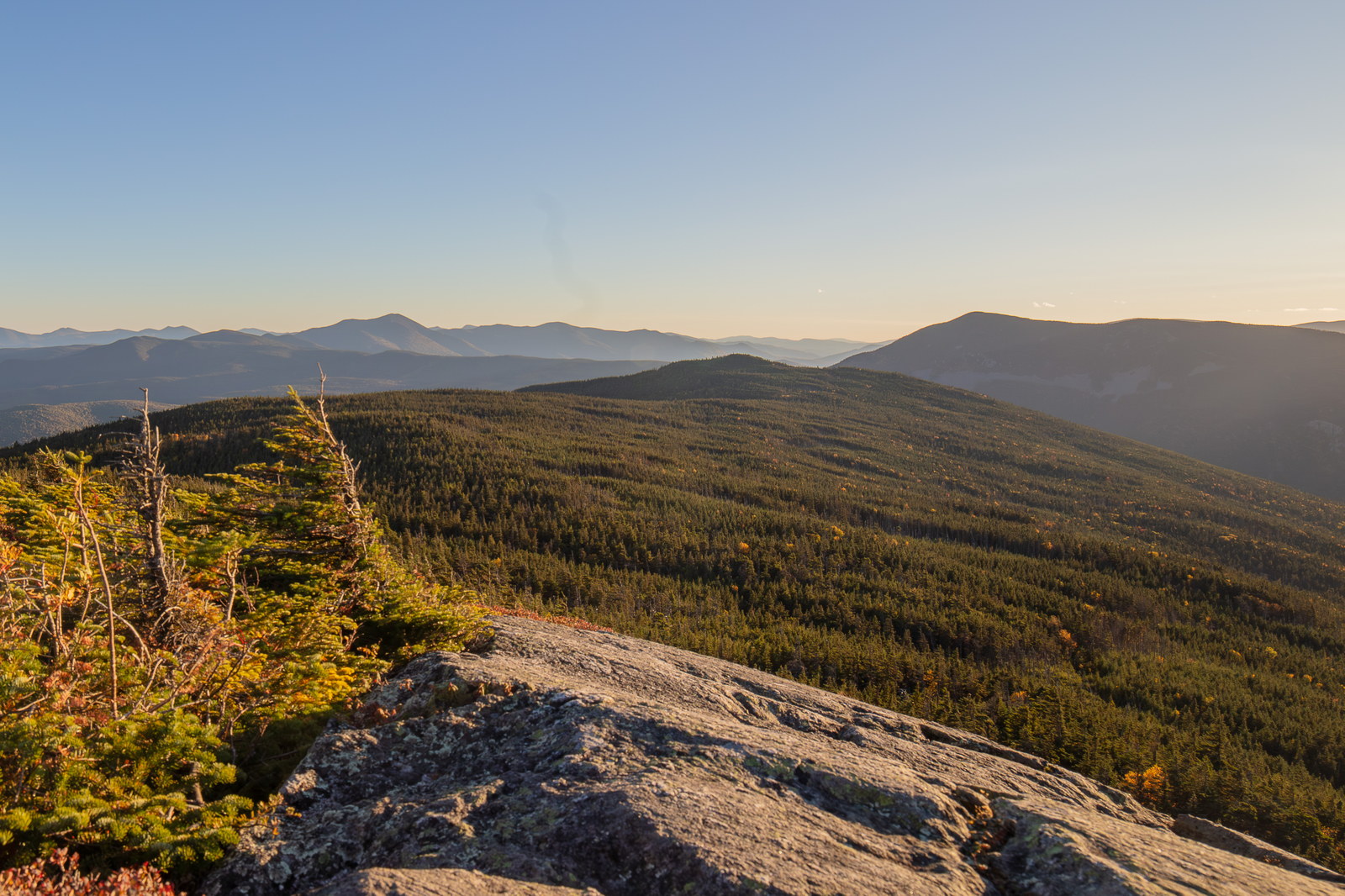 Mount Jackson rocky ledges with forest and distant ridges at sunset in White Mountains