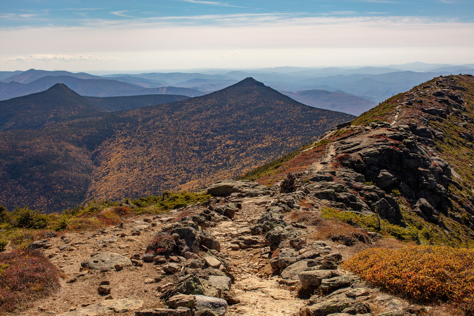 Rocky hiking trail on Mount Liberty ridge with fall foliage and distant mountain ridges