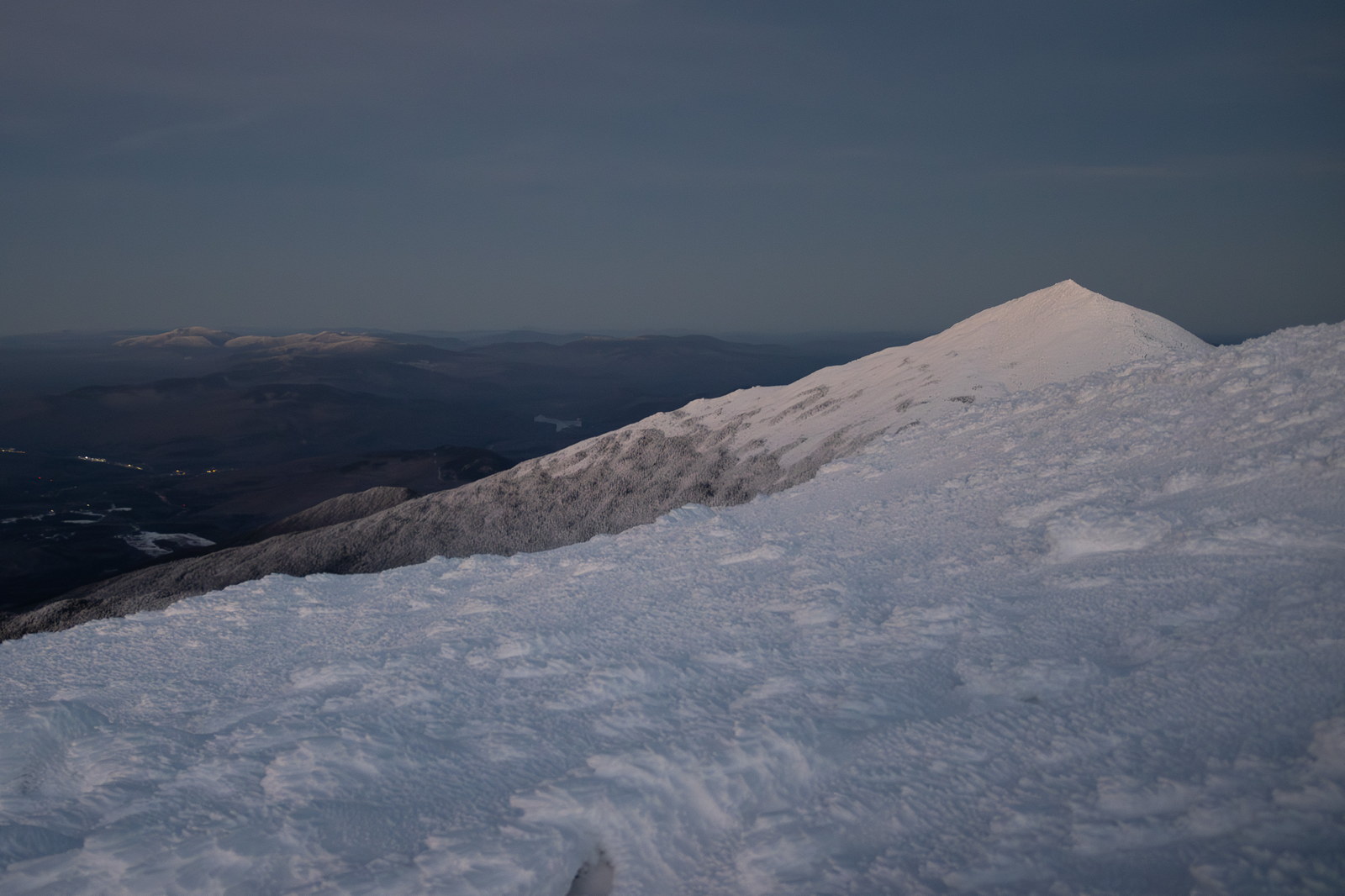 Snowy summit of Mount Madison at twilight with distant mountain ridges under clear evening sky