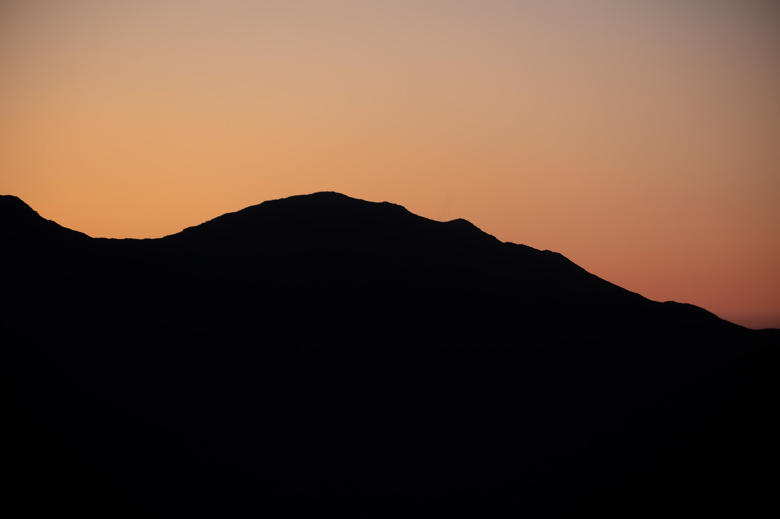 Silhouette of Mount Madison ridge at sunset with soft orange sky in White Mountains