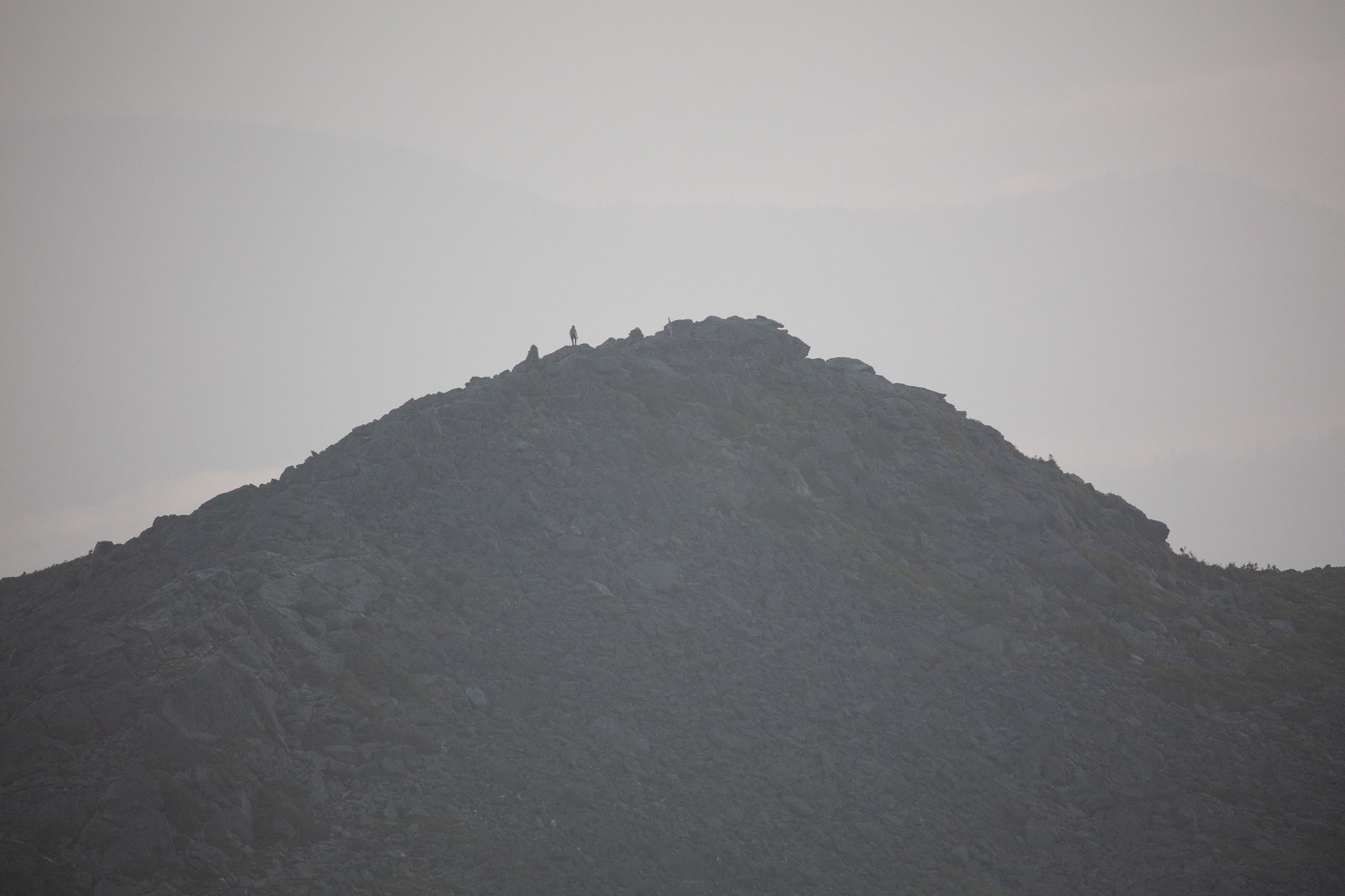 Silhouetted figure on rocky Mount Madison summit at dawn with misty background