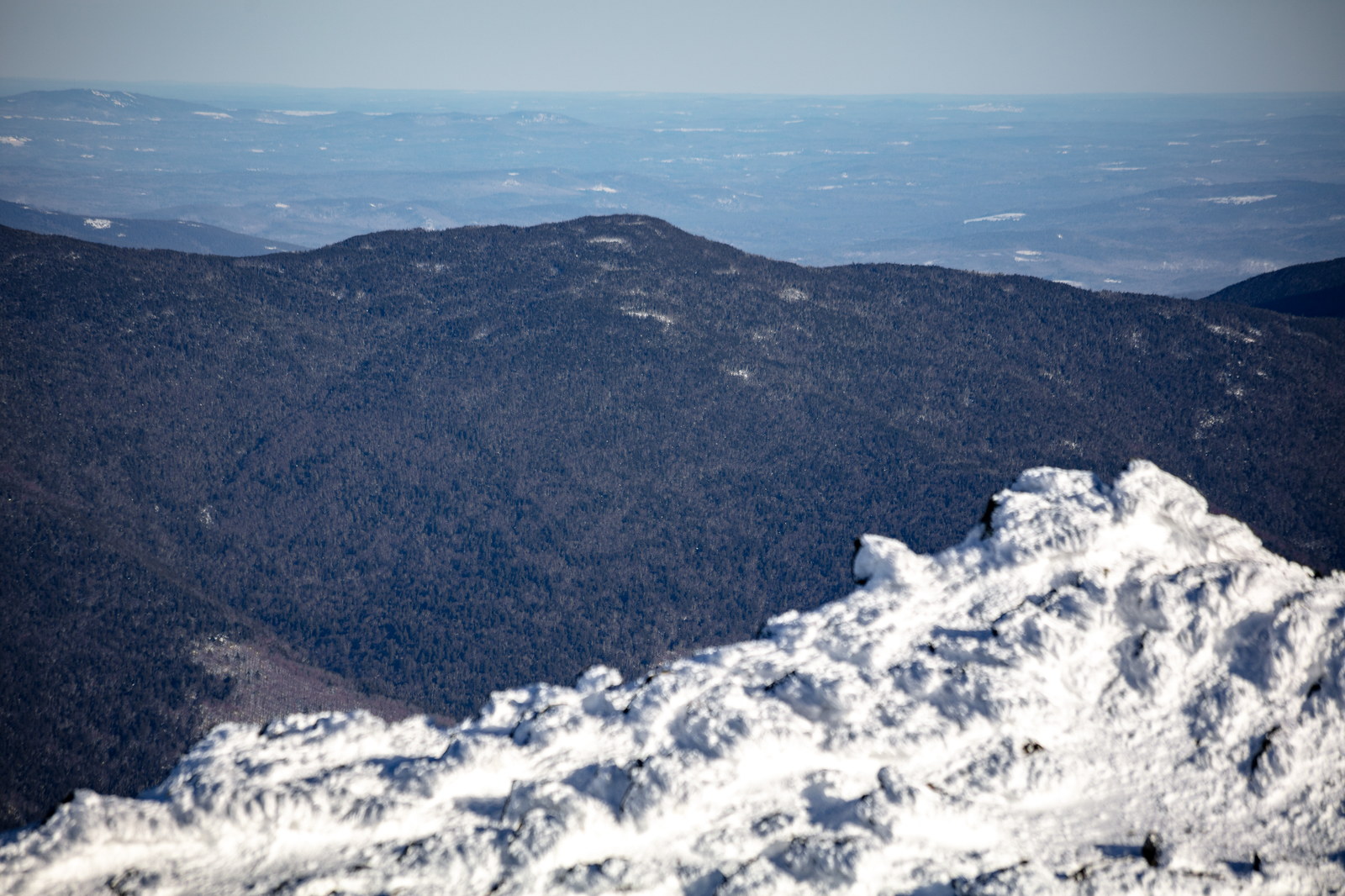 Snow-covered alpine rocks with South Carter Mountain ridge line in background under clear sky