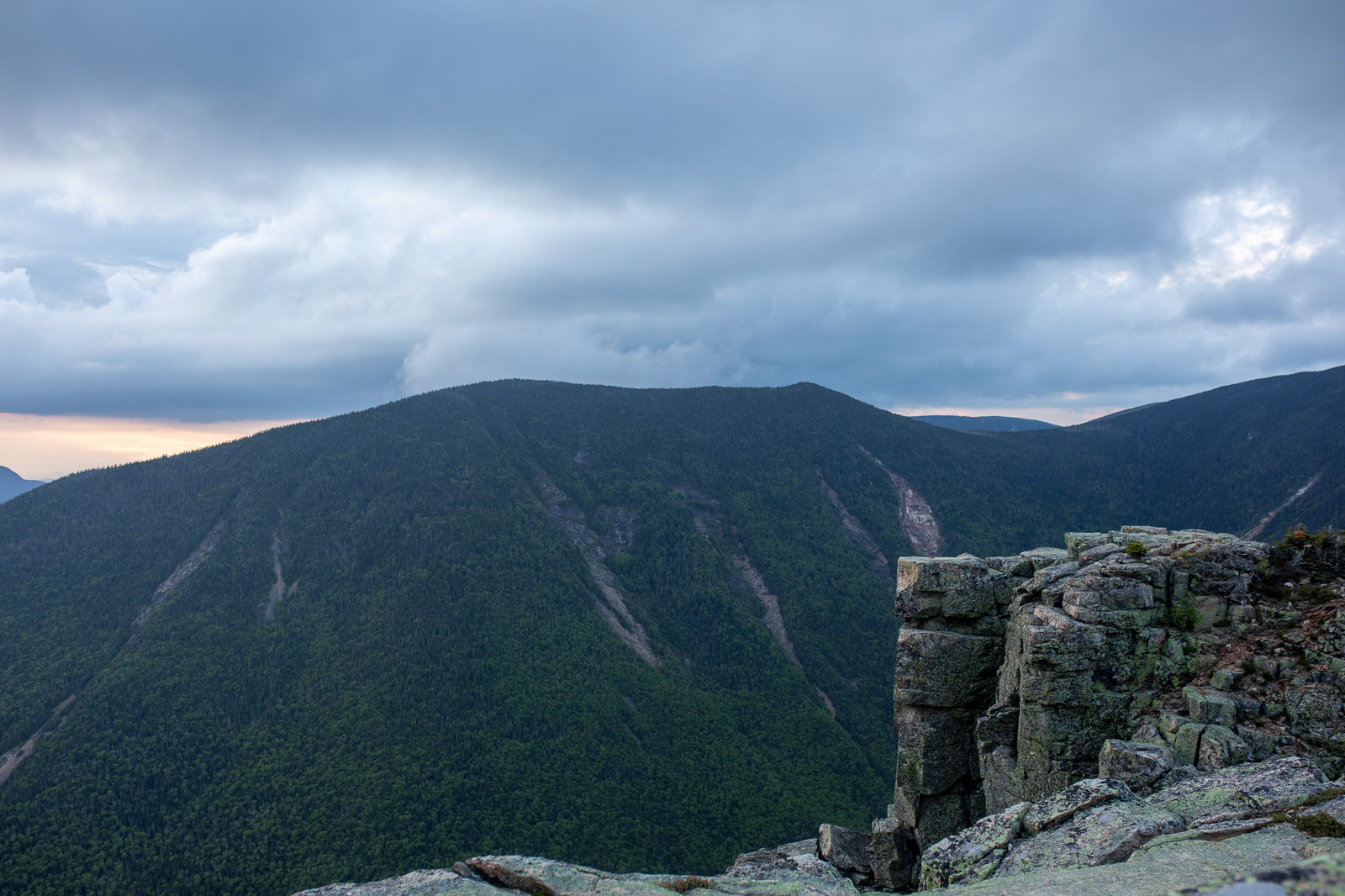 Granite rock formations and dark forested slopes of West Bond under cloudy summer sunset sky