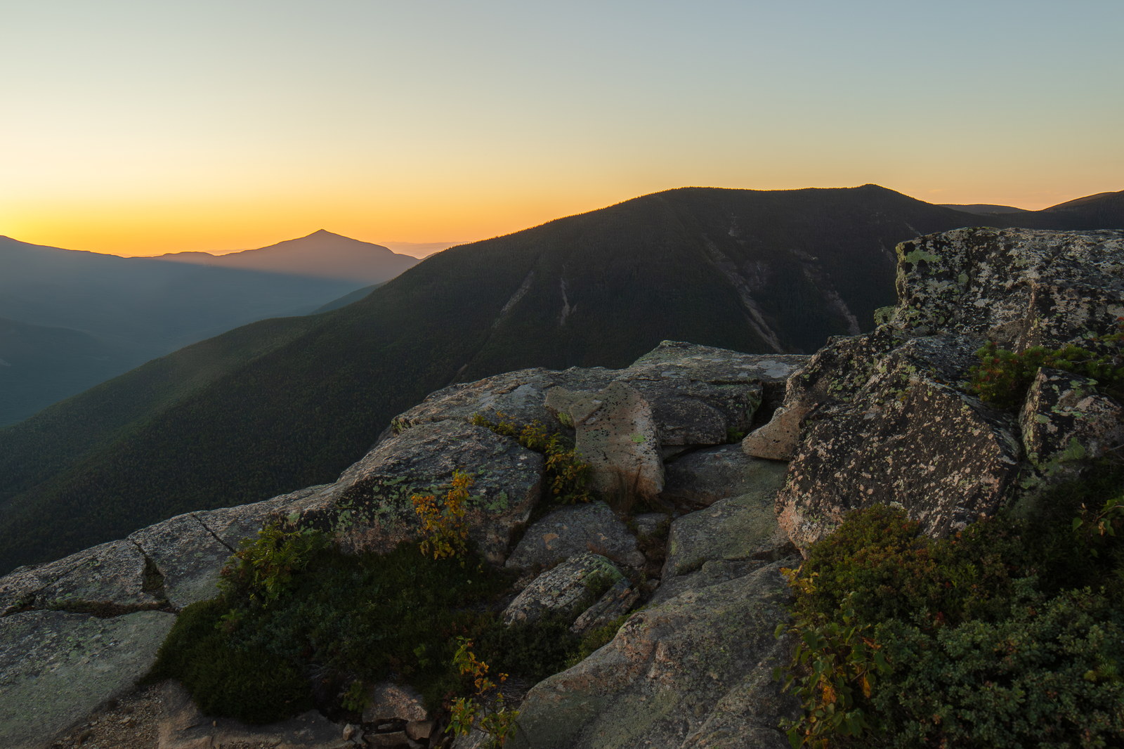 West Bond summit granite ledges at sunset with distant mountain silhouette