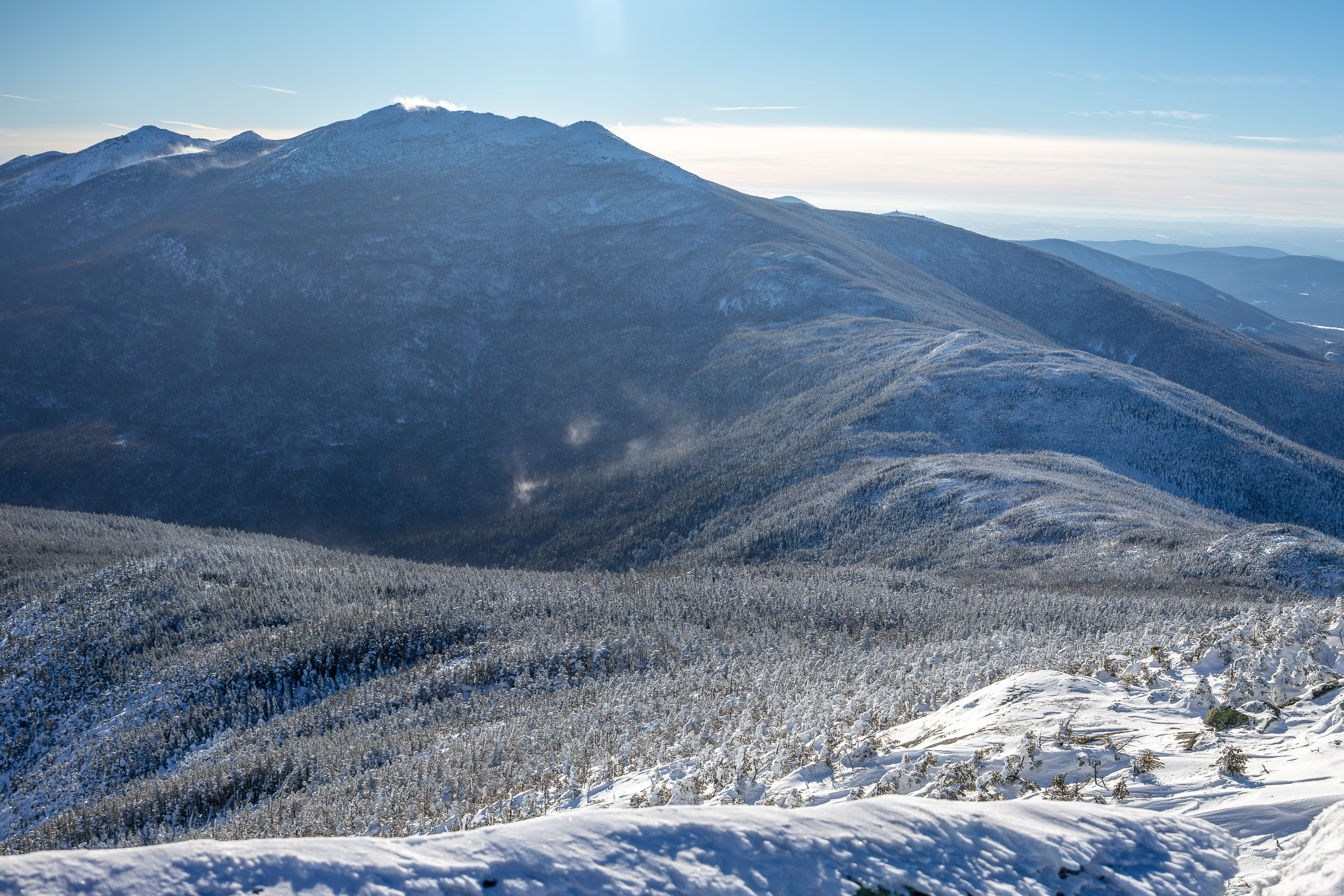 Snow-covered slopes and forested ridges of Mount Lafayette in winter under clear blue sky