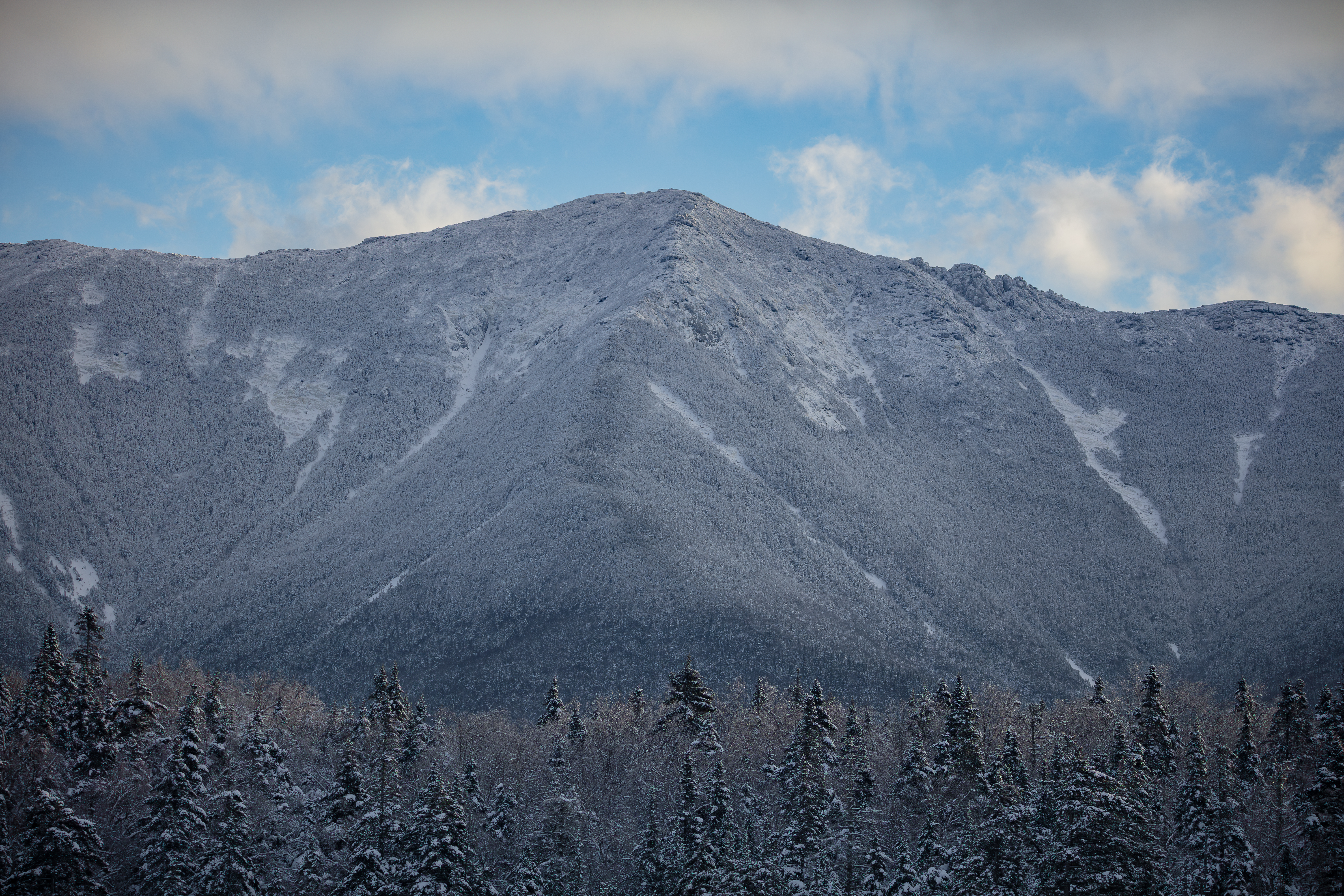 Snow-covered Mount Lincoln peak with frosted trees below under a partly cloudy sky