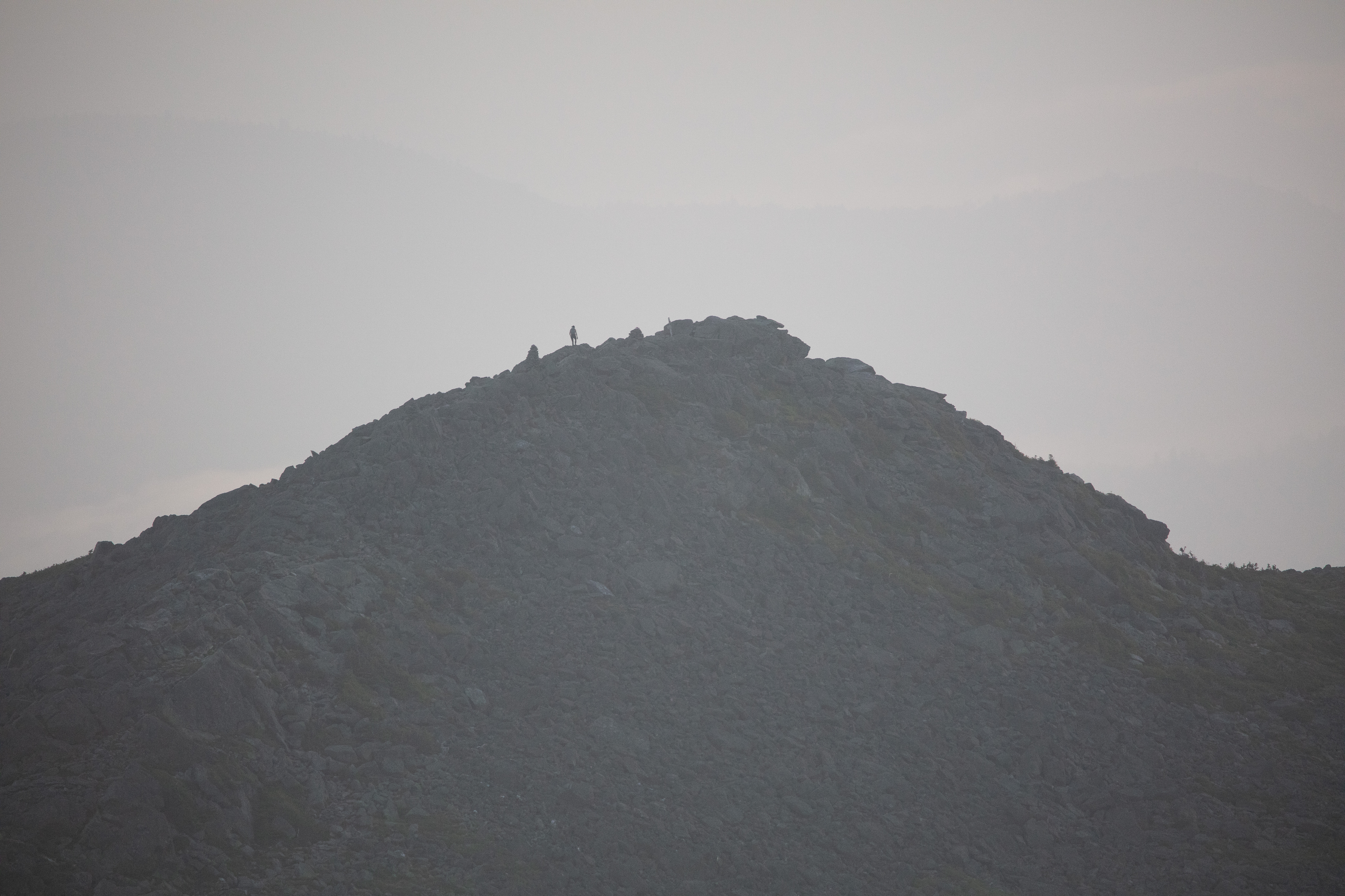 Silhouetted figure on rocky Mount Madison summit at dawn with misty background