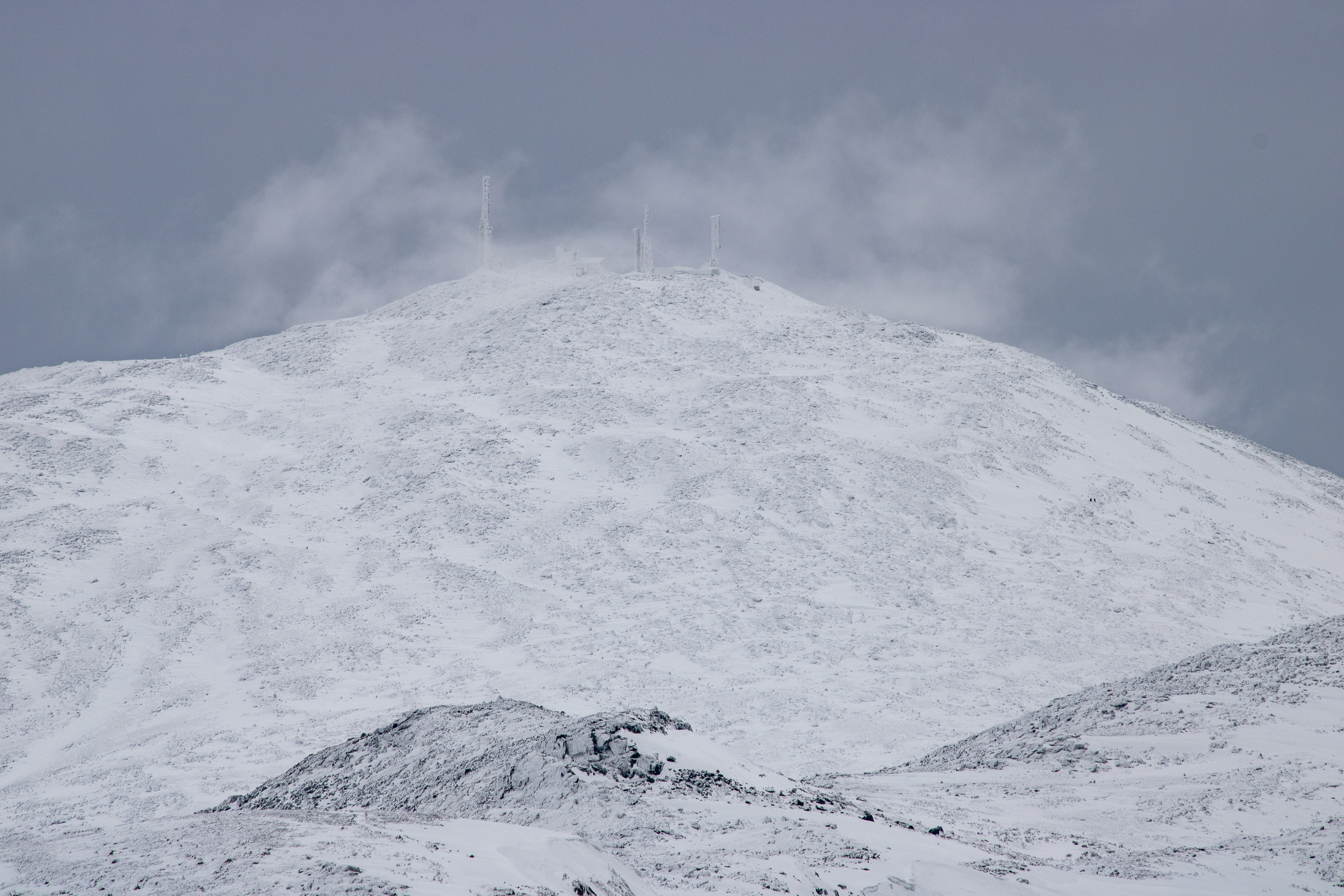 Snowy summit of Mount Washington with antennas and clouds in winter