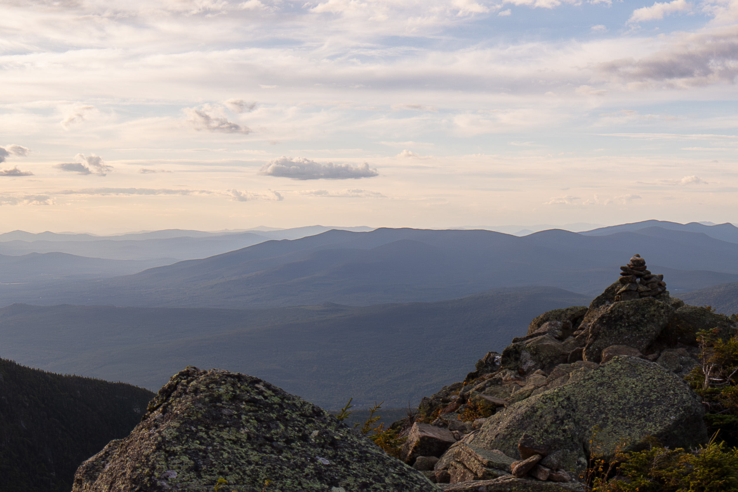 Mount Waumbek summit rocks with distant mountain ridges under soft sunset sky