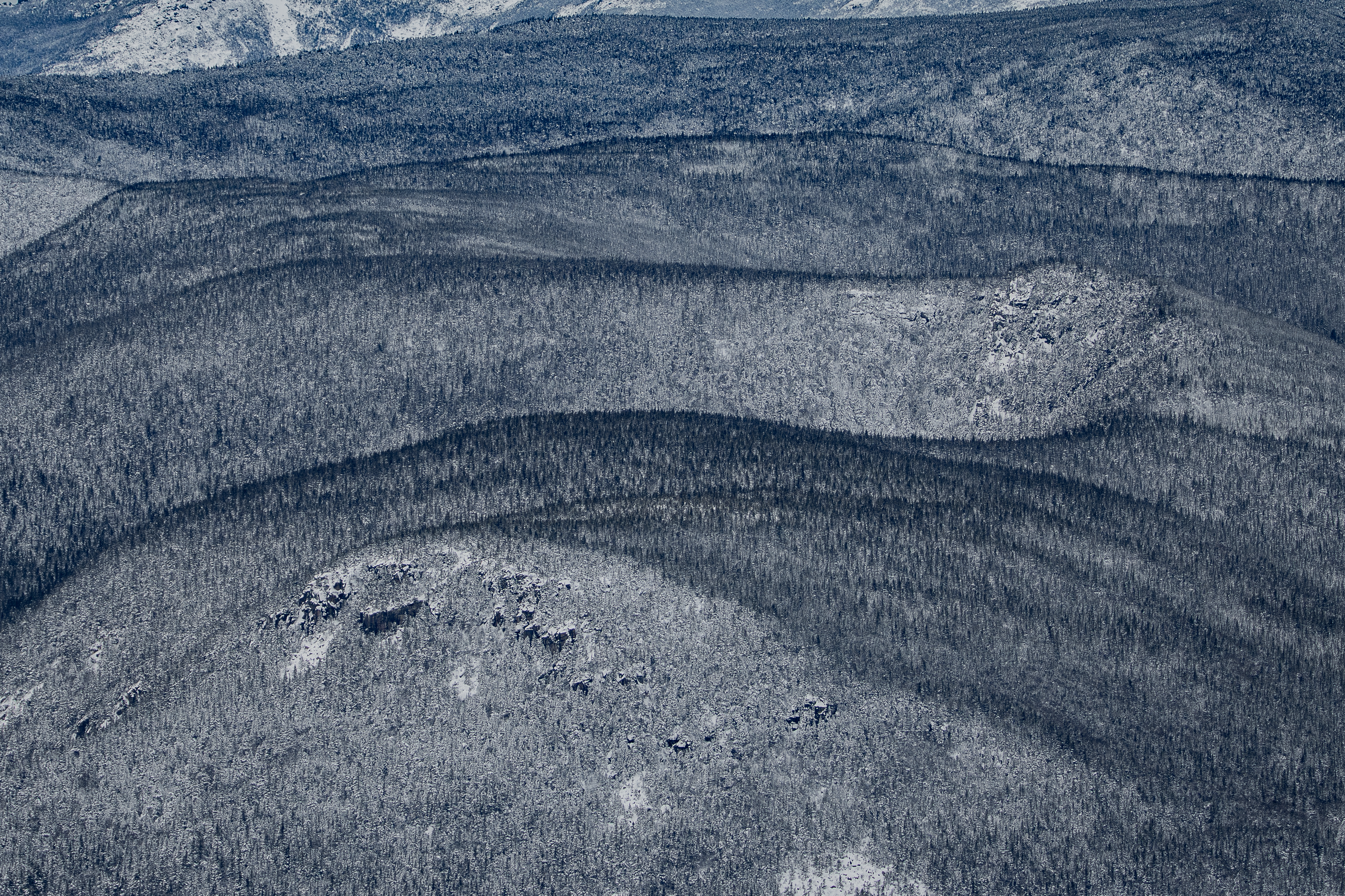 Snow-covered Zealand Mountain ridge with dense forest and granite outcrops in winter